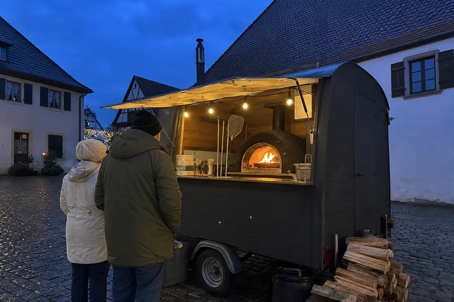 Das schwarze Pizzamobil bei blauer Stunde, in der Ausgabe leuchtet der Holzofen