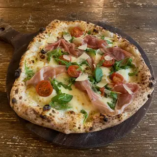 Pizzambrotta frisch aus dem Ofen, belegt mit Parmaschinken, Fior di Latte, Kirschtomaten, Rucola, Parmesanspäne, Basilikum